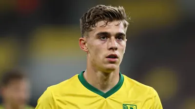 A young, athletic left-back in his early twenties, wearing a solid yellow Norwich City kit, head-and-shoulders framed...