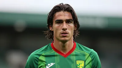 A 22-year-old Norwich City winger, athletic build, mid-thigh length dark hair, focused expression, head-and-shoulders...