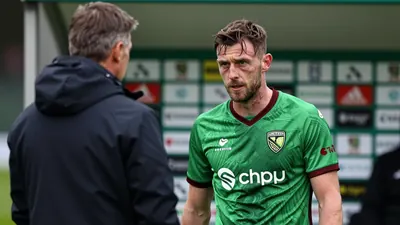 A medium shot of a rugged, 30-year-old male striker with a weathered expression, wearing Norwich City's green and dark...