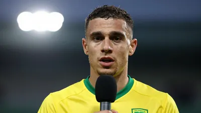A 30-year-old Norwich City player, wearing a yellow and green kit, speaking into a microphone