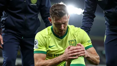 A close-up shot of a Norwich City player clutching his knee in pain, with a worried expression on his face, as he is...