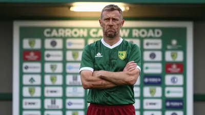 A 35-year-old, 5'10" male head coach with a weathered complexion, wearing Norwich City's home kit of a dark green shirt...