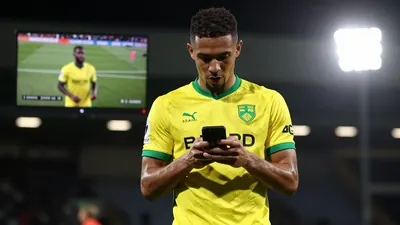 A tight waist-up shot of an anonymous Norwich City player in a yellow and green kit, looking focused and determined as he...
