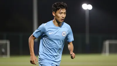 A focused 19-year-old striker in a solid light blue kit, mid-stride on a training pitch