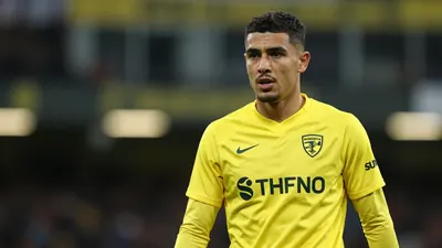 A 22-year-old male footballer in a bright yellow Norwich City training kit, waist-up, focused expression, background...