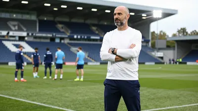 A 35-year-old, 5'10" tall, balding, bearded, and bespectacled Norwich City coach, wearing a white, long-sleeved, cotton...
