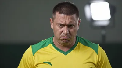 A 35-year-old male coach with a strong build, wearing a yellow and green kit, looking frustrated, with a shallow depth of...