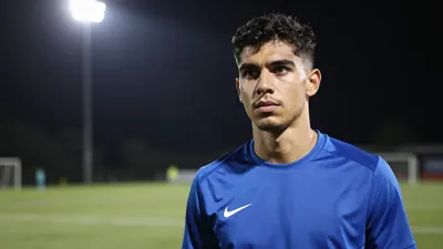 A 23-year-old winger with a muscular build, wearing a solid blue training top, standing on a football pitch with a...