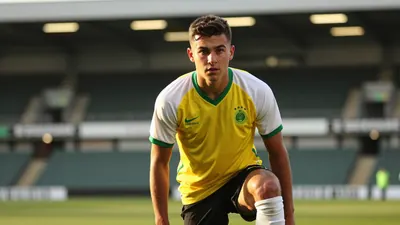 A tight, waist-up shot of a young, athletic-looking player in a yellow and green kit, with a white shirt and black...