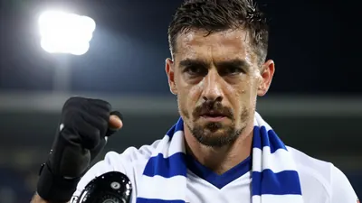 A 35-year-old centre back in a white Millwall jersey with a blue collar, black boots, and a blue and white striped scarf...