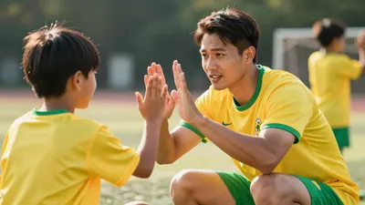 A 28-35 year old male football coach in a bright yellow and green kit, waist-up, crouching to high-five a child at a...