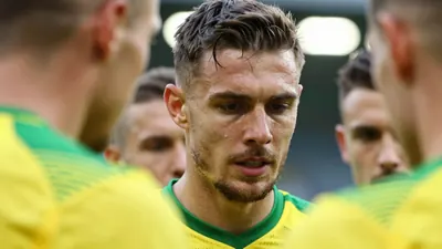 A close-up of a Norwich City player's face, with a mix of emotions on his face as he looks down at the pitch, surrounded...
