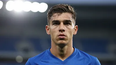 Photorealistic head-and-shoulders of a lean 19-year-old striker in a solid bright blue jersey, sharp focus on his...