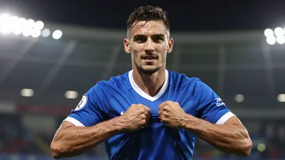 A 25-year-old muscular left-back in a solid blue jersey, celebrating his signing with a determined expression