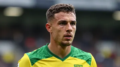 A close-up shot of a Norwich City player in a yellow and green jersey, with a determined look on their face, taken with a...