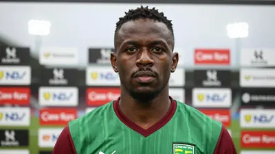 A close-up shot of a 30-year-old African male football agent, dressed in Norwich City's home kit, the green shirt with...