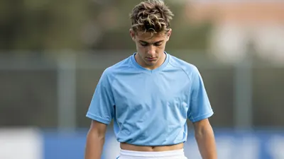 A 22-year-old, Argentine, Bologna winger with a messy, sandy-brown haircut, wearing a light blue, cotton jersey with a...