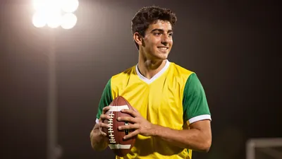 A tight waist-up shot of a young, anonymous, dark-haired player in a yellow and green jersey with a white collar, smiling...