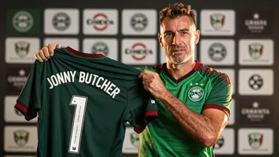 A tight, waist-up shot of a middle-aged, ruggedly-built Brazilian footballer, wearing the Norwich City home kit in green...